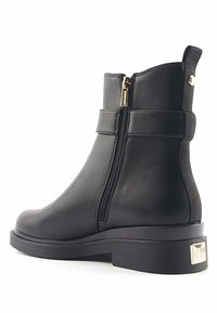 Botas negras hasta el tobillo de cuero suave, con cremallera lateral, tacón en bloque y correas decorativas en la parte superior. Suela de goma texturizada.