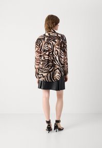 Blusa con stampa animalier in tonalità di marrone e nero, tessuto semi-trasparente, maniche lunghe e vestibilità rilassata. Abbinata a una gonna di pelle nera.