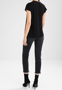 Haut noir à manches courtes avec une coupe droite, associé à un jean en denim noir. Les chaussures sont des bottines à talons aiguilles de style chaussette noir.