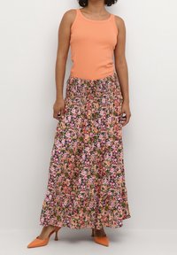 Débardeur orange associé à une jupe maxi fleurie avec des motifs roses, violets et verts ; complété par des chaussures à talons hautes orange.