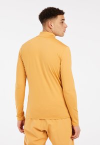 Dlhý rukáv, košeľa v horčicovo žltej farbe, vyrobená z hladkej, elastickej látky. Má vzor s vyšším golierom a priliehavý strih bez viditeľných zapínaní.