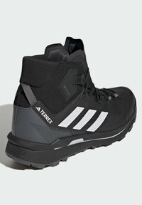 Czarne buty górskie z wysokim wsparciem kostki, z teksturowaną siateczką, białymi paskami akcentującymi oraz gumową podeszwą zapewniającą przyczepność.