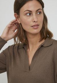 Haut en tricot marron avec col, présentant un design à encolure en V et une texture lisse. La vue en gros plan met en évidence le tissu et les détails de l'encolure.