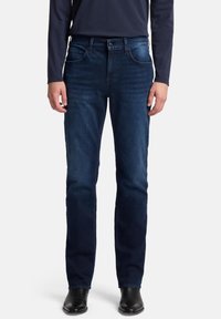 Jeans in denim blu scuro con taglio a gamba dritta, caratterizzati da cinque tasche e cuciture bianche a contrasto, abbinati a stivali in pelle nera.