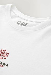 Hvid t-shirt med korte ærmer, der har et blomsterprint i rød og sort. Rund hals med glat overflade, mærket "NEXT Relaxed Fit."