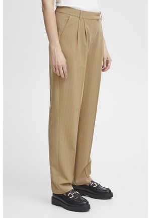 Pantalons beige à rayures avec une coupe décontractée, dotés d'une taille haute, d'un devant plissé et d'une coupe au niveau des chevilles. Accompagnés de mocassins noirs.