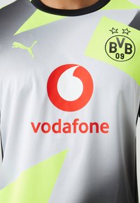 Maglia sportiva grigia con accenti verde neon, caratterizzata da un prominente logo rosso Vodafone e un logo nero Puma. Presenta l'emblema BVB 09 con due stelle.