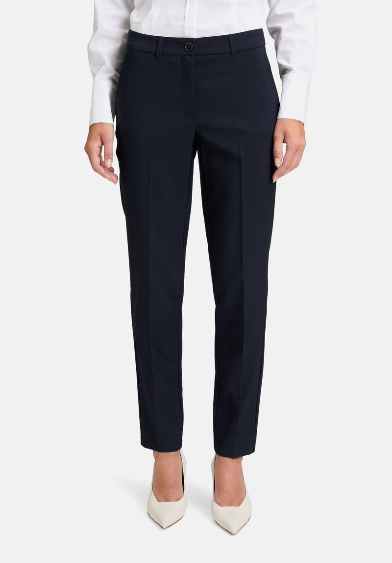 Marina blå byxor med skräddarsydd passform, i ett mjukt tyg, med bälteshällor, sidofickor och en veck ner fram; parat med vita klackar.
