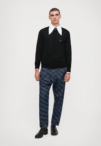 Black sweater with a white collar, blue patterned pants, and black shoes. Sweater features a small logo on the chest.