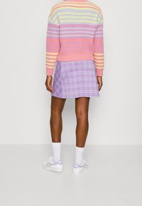 Pull rayé pastel rose, jaune et lavande ; mini-jupe en tartan lavande ; chaussettes blanches ; baskets blanches avec des touches de lavande.