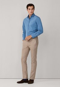 Svijetloplena košulja s kragnom, u kombinaciji s bež hlačama teksture i smešnim nubuk cipelama. Jednostavan dizajn, bez vidljivih uzoraka.