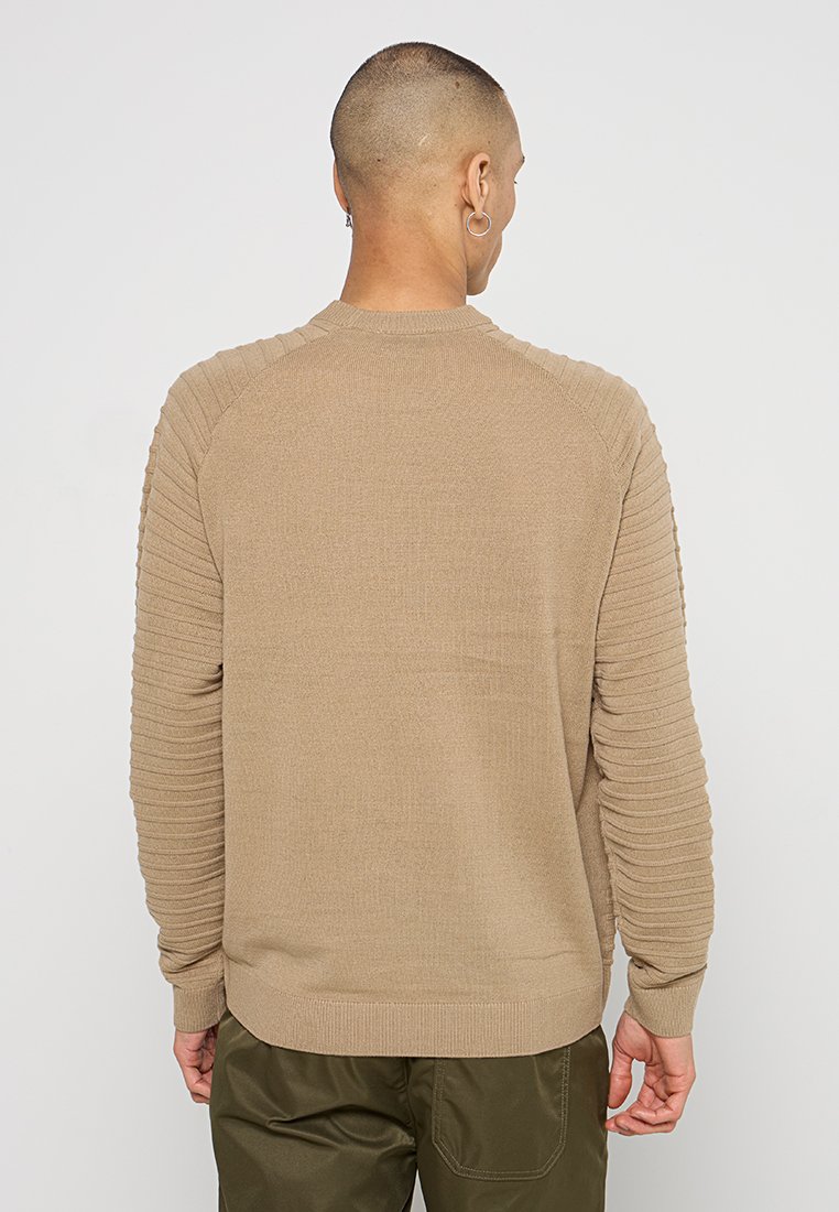 Suéter de punto beige con textura acanalada en las mangas, cuello redondo y un ajuste relajado. La vista posterior muestra una tela suave sin patrones.