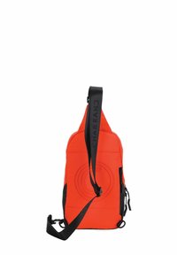 Sac bandoulière en tissu rouge avec une sangle noire. Présente un design circulaire en relief sur le devant et une poche zippée latérale. Forme compacte et angulaire.