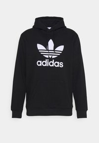 Svart hoodie i bomullsmix, med en känguruficka, snörning i huvan och en stor vit adidas-logga med tre ränder.