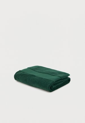 Toalla de baño verde oscuro doblada con una franja texturizada cerca del borde sobre un fondo blanco.