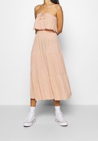 Robe maxi florale pêche avec un haut à volants superposés, une taille élastique et une jupe ample et fluide, associée à des baskets montantes blanches.