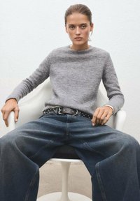 Sivi pleteni pulover s okroglim izrezom, v kombinaciji s širokimi modrimi kavbojkami. Obleka vključuje poudarek s črnimi pasom z žebljički.