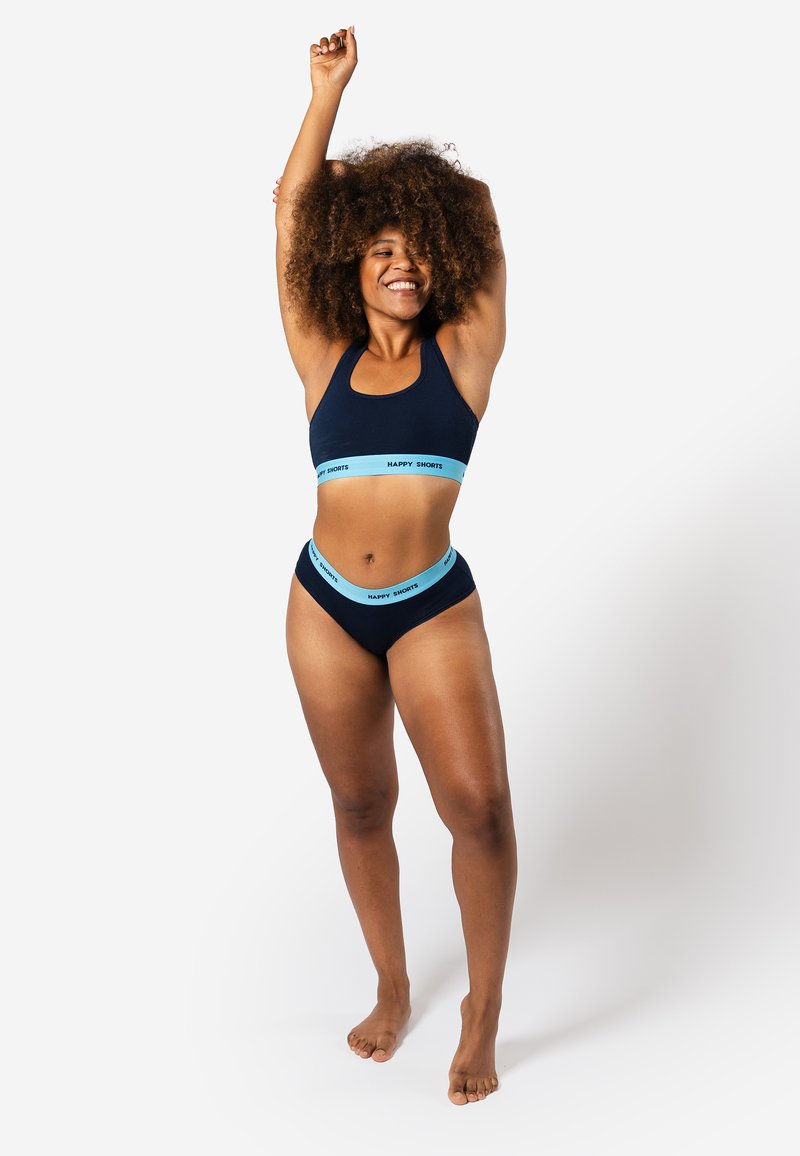 Ensemble de maillot de bain et de soutien-gorge de sport bleu marine avec des bandes élastiques bleu clair étiquetées "HAPPY SHORTS". Le tissu semble doux et extensible.