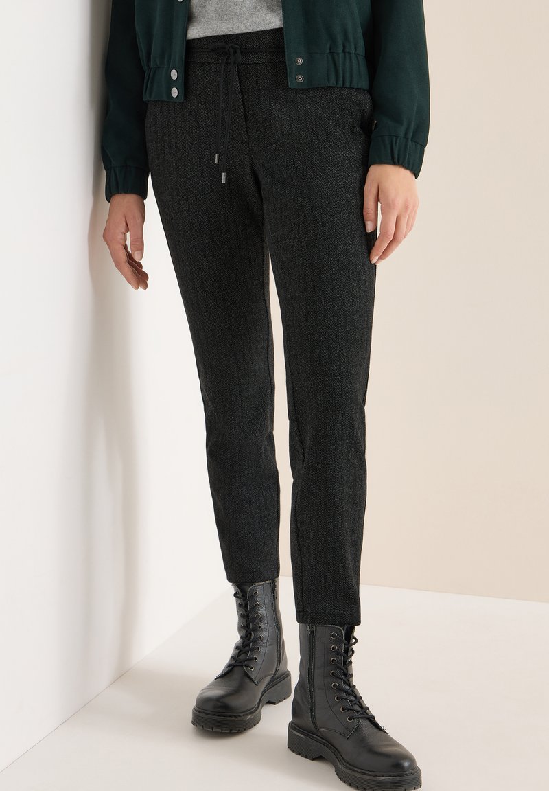 Černé tapered kalhoty vyrobené z texturované látky, s elastickým páskem na stažení. V kombinaci s černými šněrovacími bojovými botami.