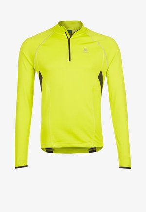 Camiseta deportiva de manga larga en color amarillo neón con paneles laterales negros y una cremallera corta negra en el cuello.