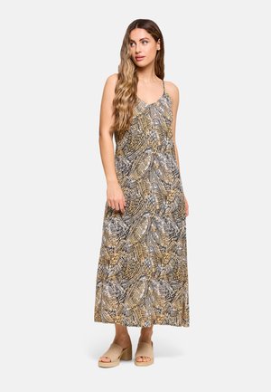 Mujer con cabello largo y ondulado que lleva un vestido maxi sin mangas con un patrón abstracto de hojas en beige, negro y blanco, y sandalias beige con tacón ancho.