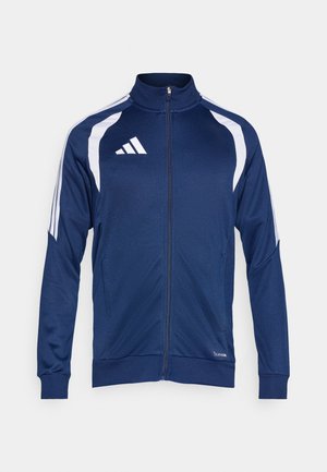 Chaqueta deportiva azul marino con detalles blancos. Cierre frontal completo con cremallera, cuello alto y bolsillos laterales. Presenta tres rayas blancas en los hombros. Textura suave.