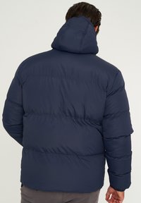 Marineblaue Steppjacke mit Kapuze, mit Steppnähten und elastischen Bündchen, aus einem glatten, wasserabweisenden Material gefertigt.