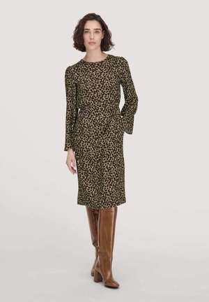 Olifantenprint jurk in olijfgroen, lange mouwen, ronde hals, middellange lengte en zijzakken, gecombineerd met bruin kniehoge haklaarzen.