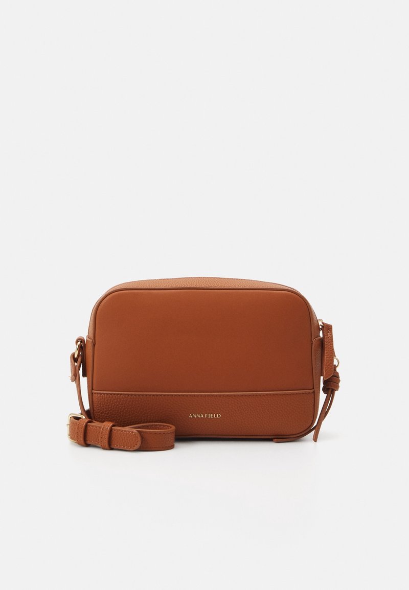 Brown faux leather crossbody bag, rectangular shape, smooth texture with pebbled accents, adjustable strap, brand name in gold lettering.