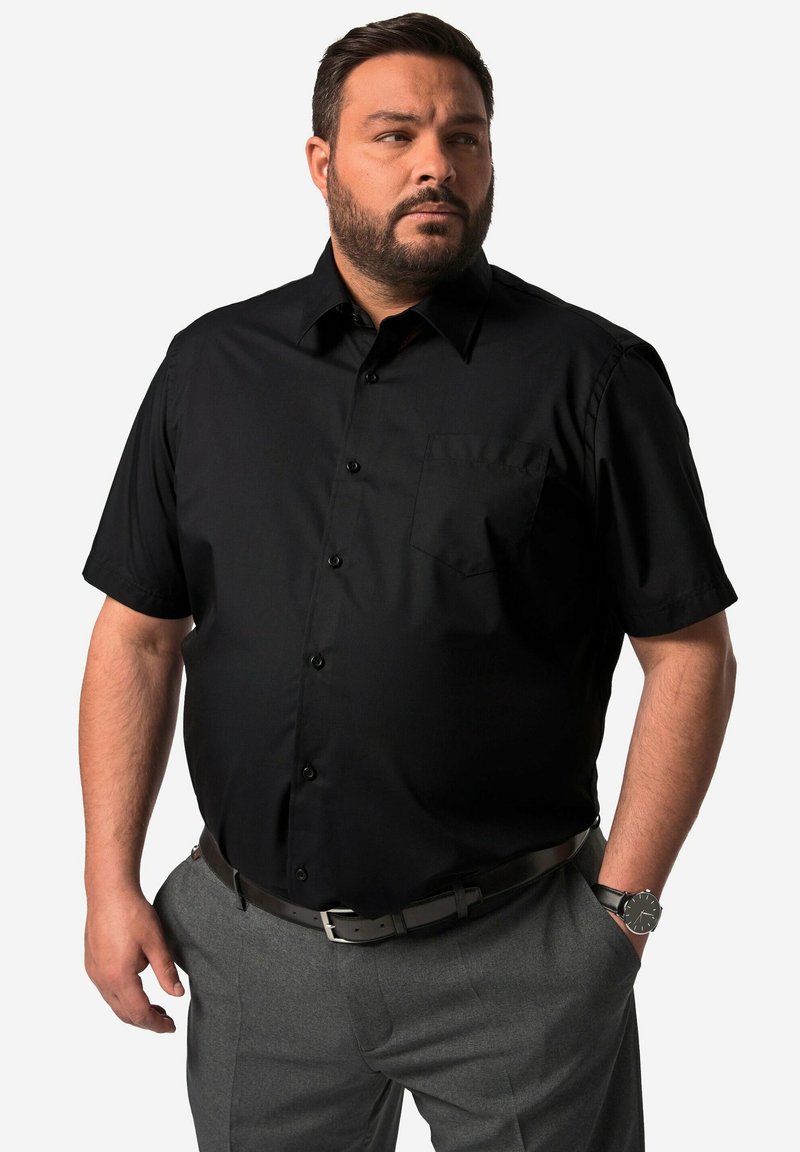 Camisa negra de manga corta con botones y un bolsillo en el frente, fabricada con material suave, combinada con pantalones grises y un cinturón negro.