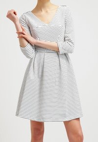 Randig klänning i vitt och svart. V-ringning, trekvartsärmar, figursydd midja, utsvängd kjol. Mjuk tyg, horisontella ränder.