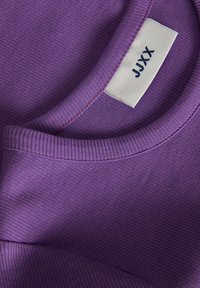 Violetti ribbikuvioinen collegepaita, jossa on pyöreä kaula-aukko, kontrastiväriset saumat ja kauluksessa brändin nimi sisältävä etiketti.