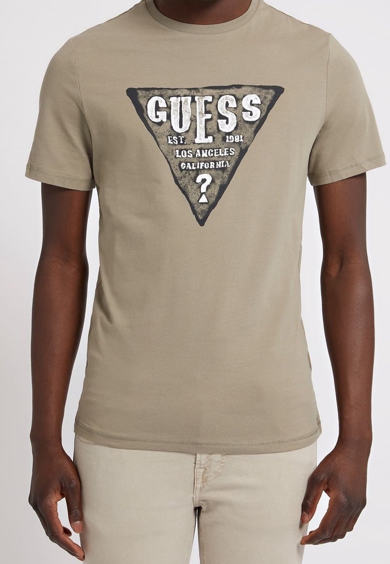 Camiseta de algodón verde oliva con un gráfico triangular en blanco y negro que incluye "GUESS" y detalles de la ciudad. Mangas cortas, cuello redondo, diseño ajustado.