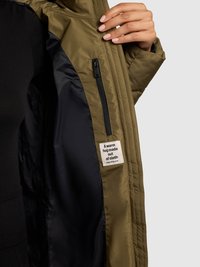 Olivevärvi paks jope sisu, millel on must vooder, tõmblukuga tasku ja silt, millel on kirjas "Soe kallistus kangast." Pehme tekstuur.