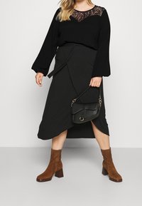 Sort top med blonde detaljer ved halsen, parret med en sort omslagsnederdel, brune ruskind blokhælede ankelstøvler og en sort håndtaske.