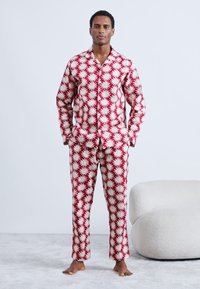 Set de pijamale roșu și alb cu model, format dintr-o cămașă cu nasturi și pantaloni cu design stelat. Material moale, croială relaxată și fără închizători vizibile.
