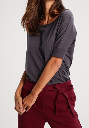 Woman wearing a loose dark gray short-sleeve top tucked into high-waisted burgundy pants with a tied waist belt.