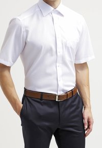 Camicia bianca a maniche corte con bottoni e tasca, abbinata a pantaloni blu scuro e una cintura in pelle marrone con una fibbia in argento.