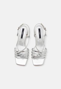 Ασημί γόβες slingback με τετράγωνη μύτη. Διαθέτουν λεπτές διασταυρούμενες ιμάντες και ιμάντα στον αστράγαλο. Λείο μεταλλικό φινίρισμα με χαμηλό τακούνι.