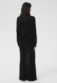 Black knitted sweater and matching skirt, featuring a loose fit, long sleeves, side slits, and a textured pattern.