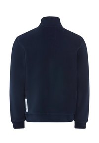 Felpa in pile blu navy con colletto alto, maniche lunghe e polsini a costine. Presenta una piccola toppa con logo sul lato sinistro.