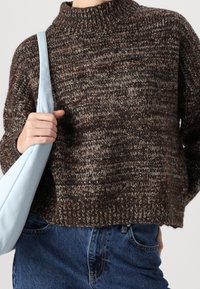 Brauner Strickpullover mit hohem Kragen, lockerem Schnitt und strukturiertem Muster. Kombiniert mit einer hellblauen Schultertasche und Jeans.