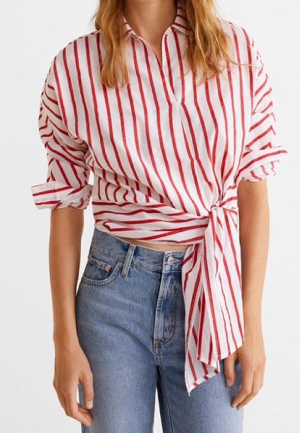 Chemise blanche à rayures verticales rouges, manches courtes retroussées, col en V, nouée à la taille ; portée avec un jean en denim bleu clair.