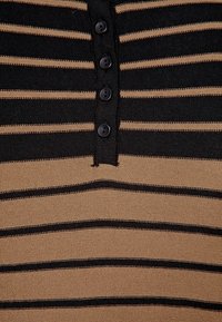 Chemise en maille rayée noir et fauve avec une patte de boutonnage à cinq boutons noirs au niveau de l'encolure et un tissu texturé.