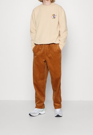 Béžová mikina s kresleným motivem, doplněná hnědými manšestrovými kalhotami a bílými teniskami se zelenými detaily.