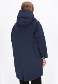 Marineblå pufferjakke med hætte. Har lige snit, lange ærmer og bagventilation. Materialet virker glat med minimal tekstur.