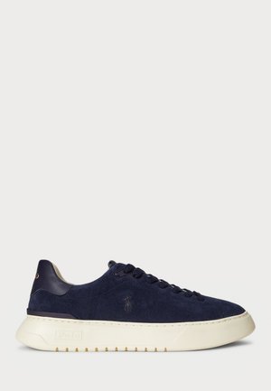 Low-top navy blue suede sneaker with white thick sole, lace-up front, and small embossed logo on side.