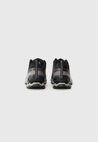 Zwarte trailrunschoenen met een grijze tussenzool en een getextureerde rubberen buitenzool. Kenmerken zijn onder andere een verstevigde hiel en reflecterende accenten.