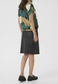 Kortärmad topp med färggård abstrakt mönster i grön, beige och guld; matchad med en svart skinnpencilkjol. Svarta skor fulländar looken.