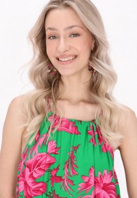 Ziedu halter tops dzīvīgā zaļā krāsā ar rozā tropiskajiem ziedu rakstiem. Viegls audums ar savilkta dekoltē līniju un plānām plecu siksnām.
